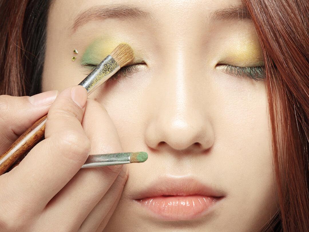 Close-up of makeup artist's hand applying yellow and green eyeshadow to an Asian woman's eyelid Desktop