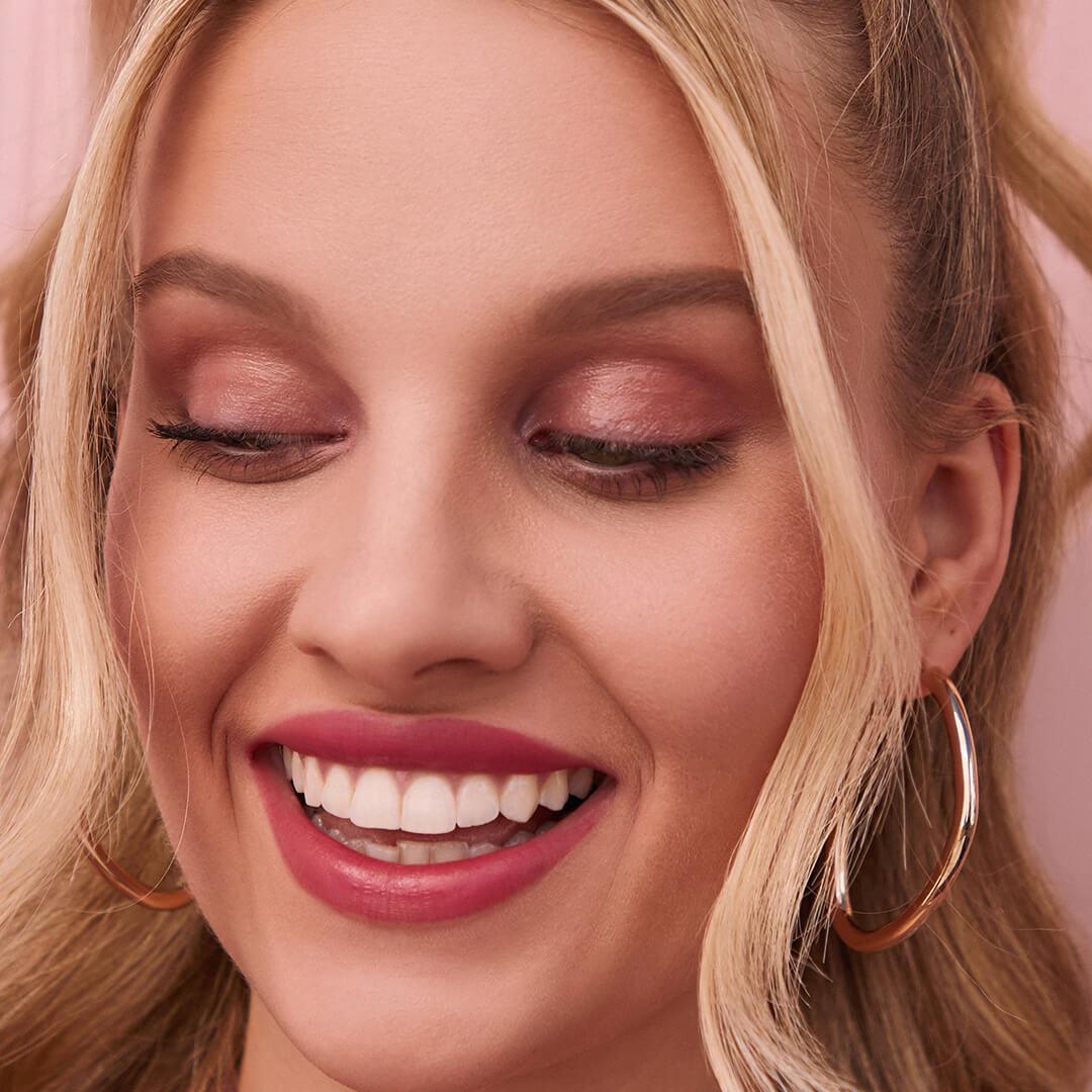 An image of a model wearing subtle red eyeshadow in her crease. Mobile