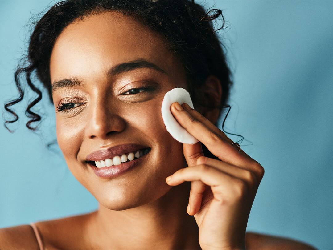 Smiling woman applying toner with a round cotton pad against blue background Desktop