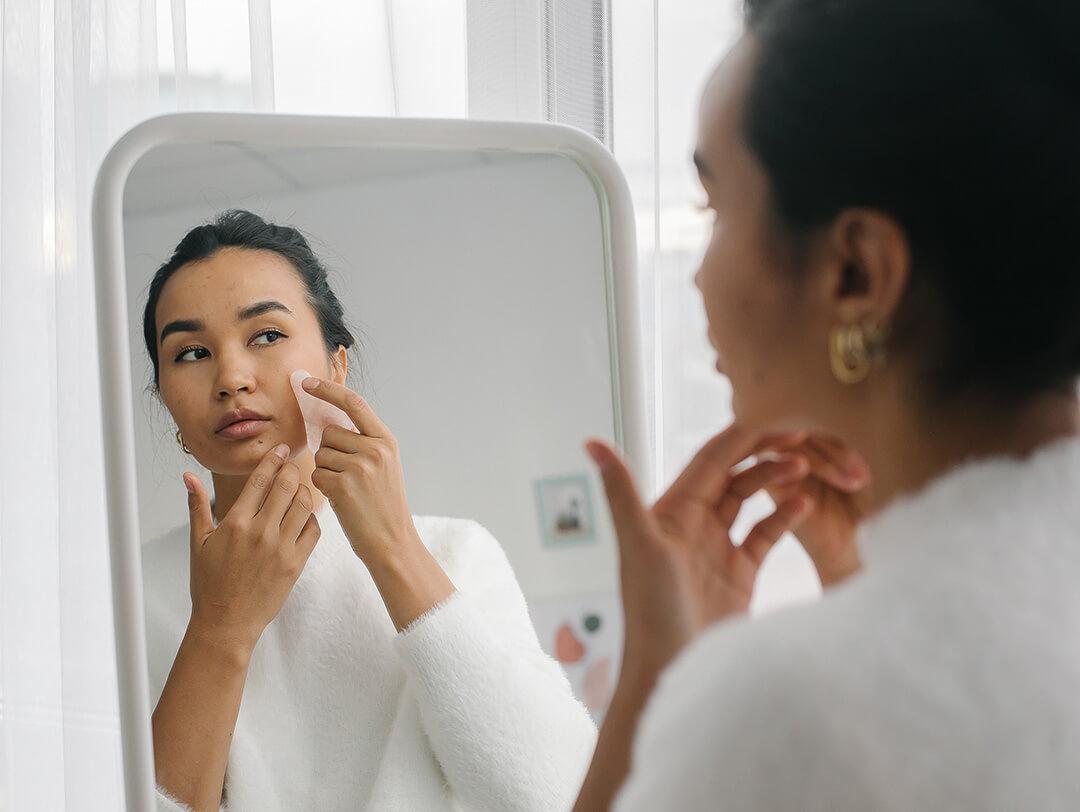 A photo of a model using gua sha on her face using a mirror Desktop