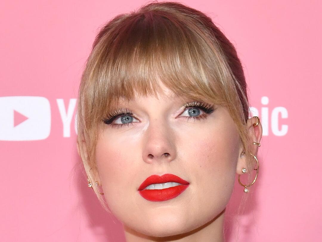 Close-up of Taylor Swift rocking neutral makeup look paired with red lips and sleek hairstyle with bangs Desktop