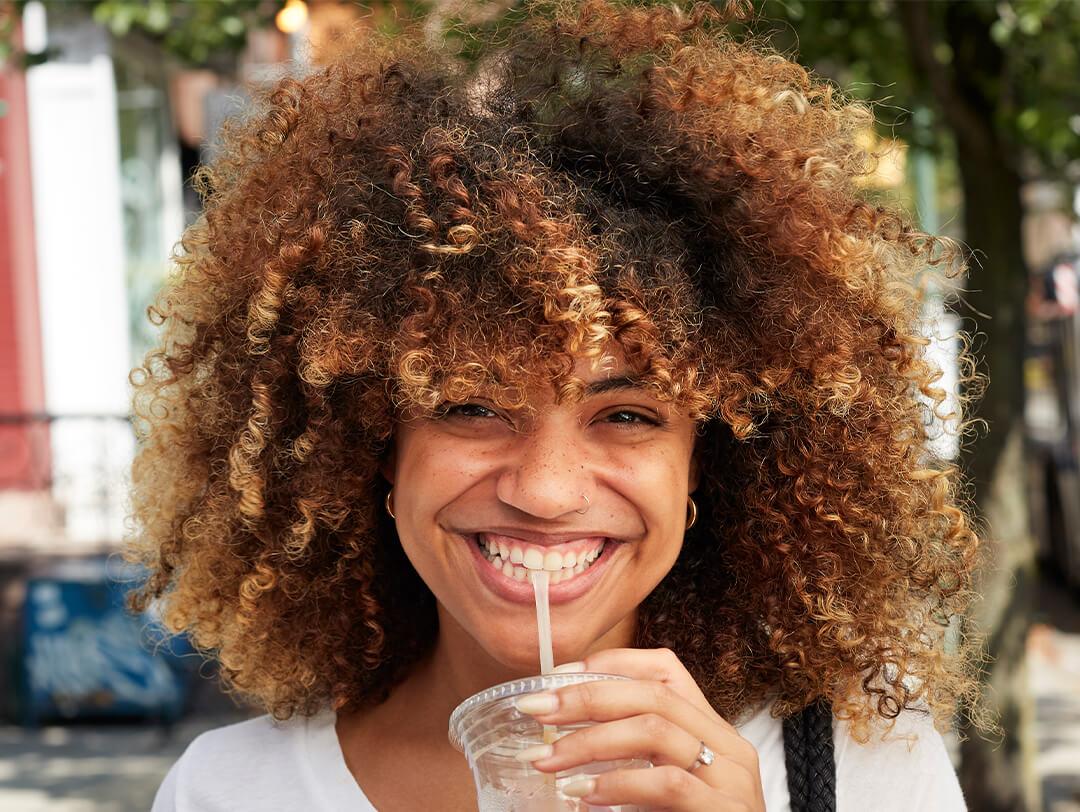 Young black woman with curly hair drinking through a straw Desktop