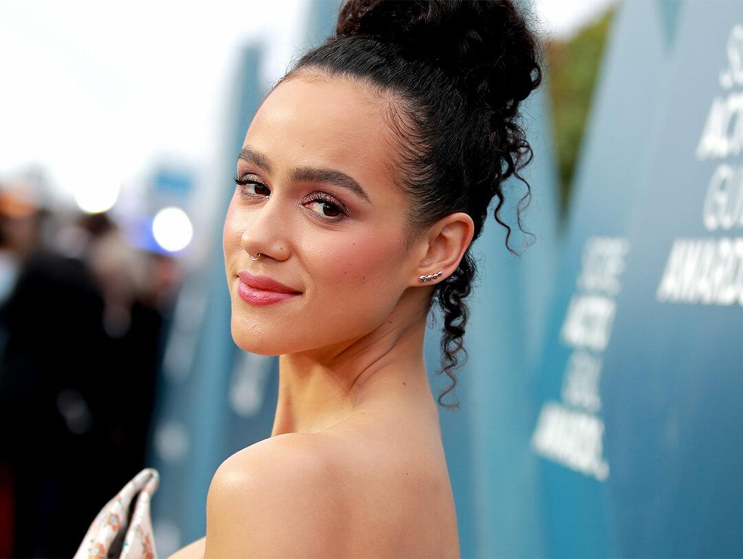 Close-up image of a glam Nathalie Emmanuel with an up-do hairstyle against aqua blue background on red carpet Desktop