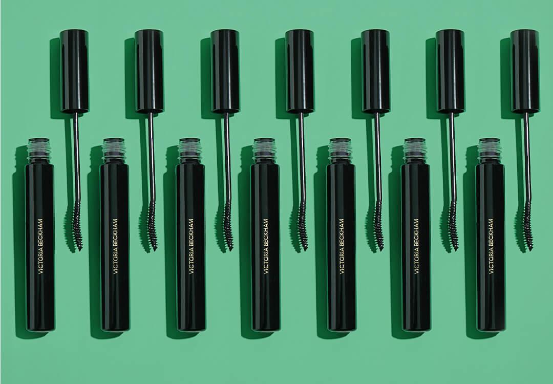Seven tubes of VICTORIA BECKHAM BEAUTY Future Lash Mascara neatly arranged on green background Desktop
