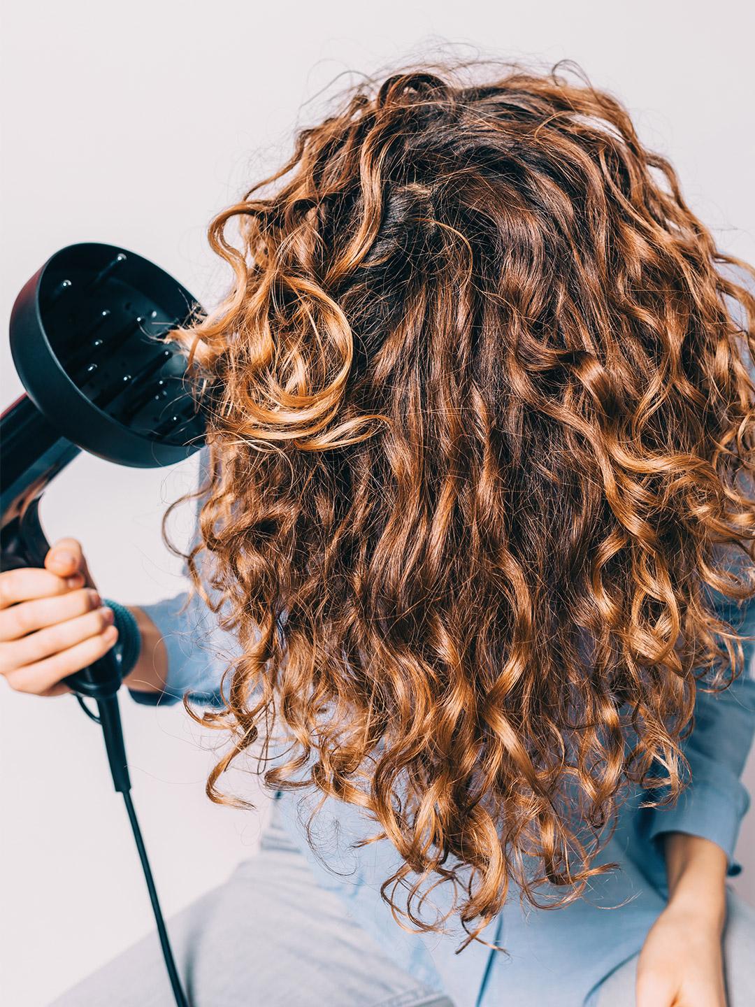 A photo of a woman sitting on chair styling her curly hair with a diffuser Desktop