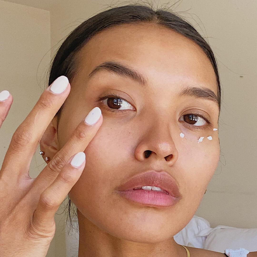 Close-up image of model with white mani putting on eye cream on clean skin Mobile