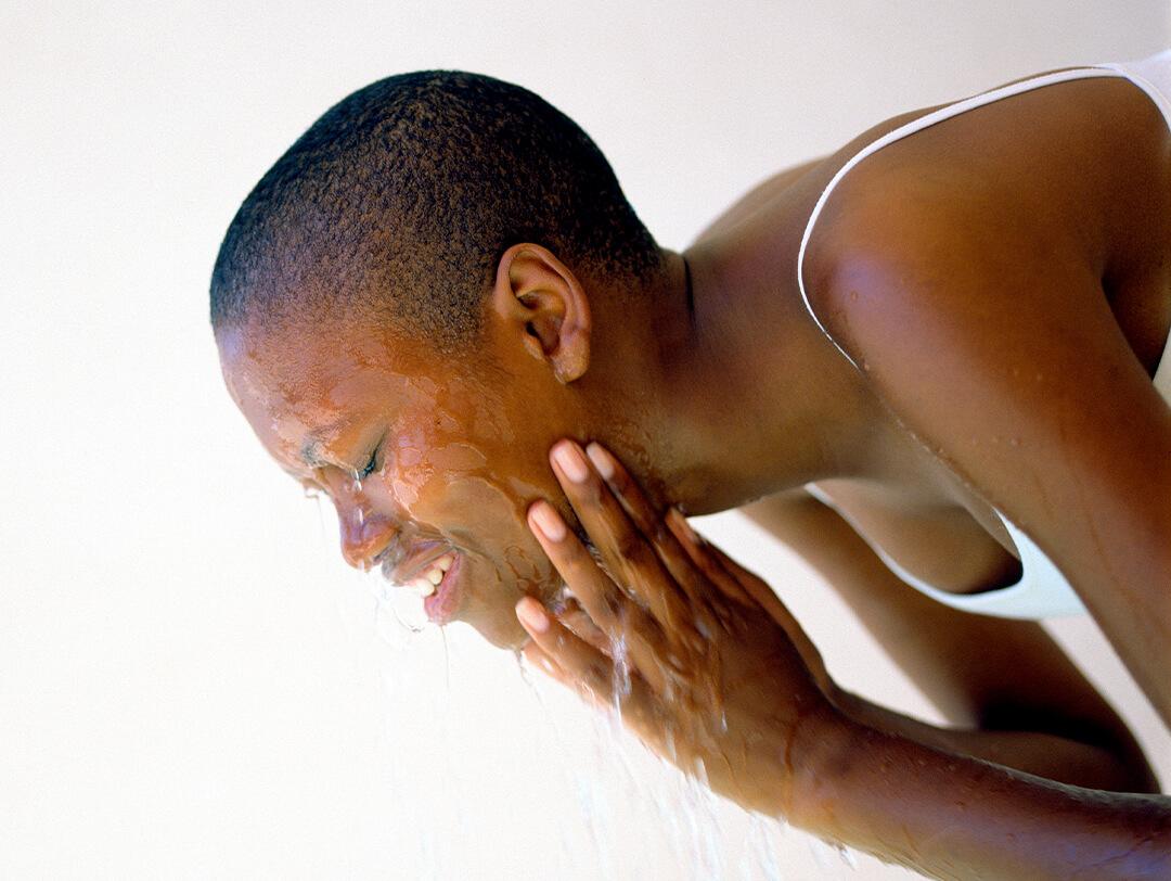 Black woman in a white tank top washing her face Desktop