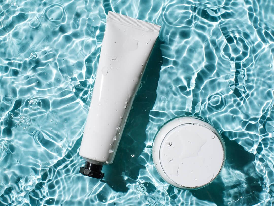 Tube and jar of skincare product partially submerged in water with waves Desktop