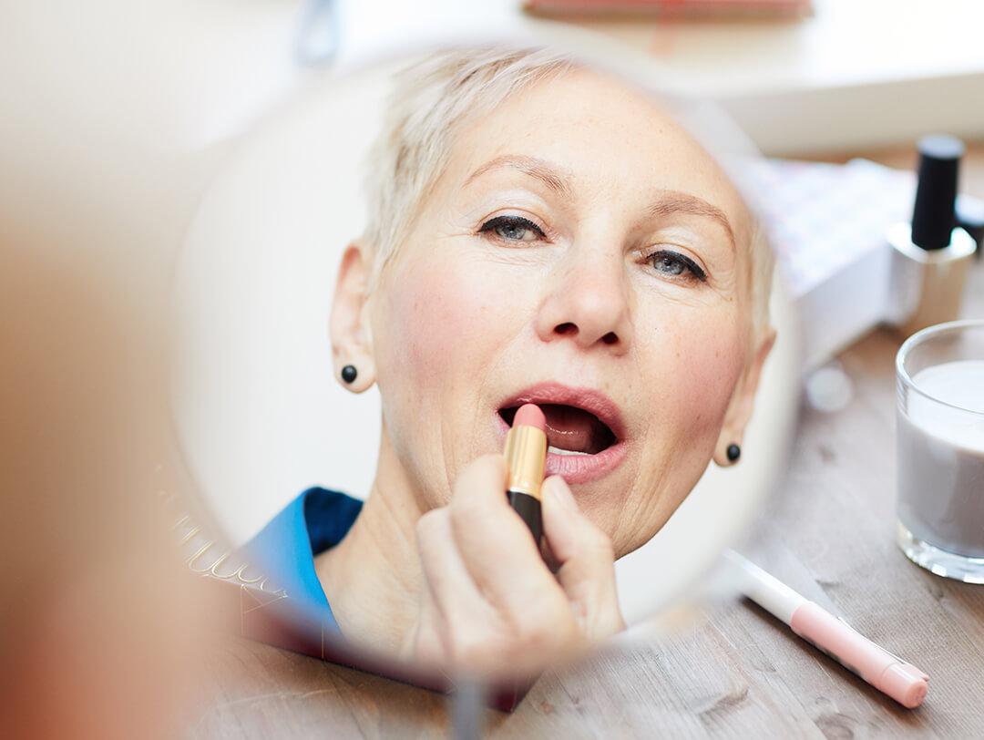 Mature woman applying lipstick while looking at a mirror Desktop