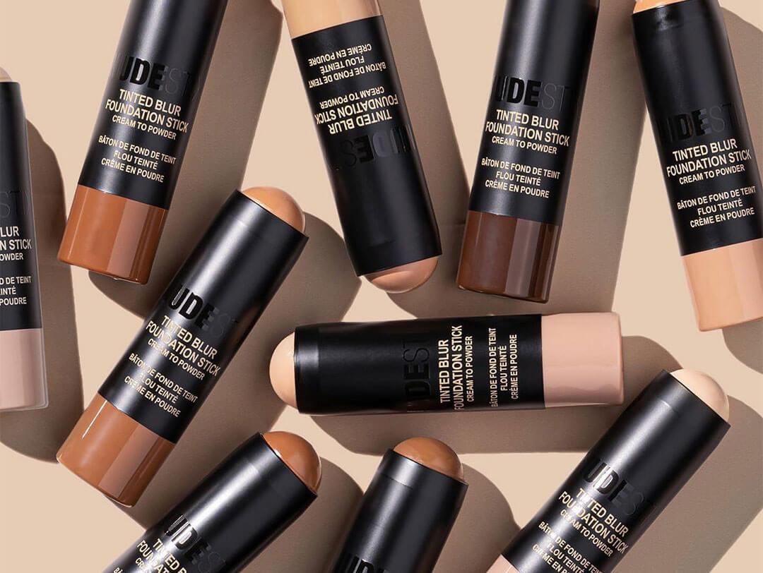 An assortment of stick foundations in various shades, perfectly arranged on a flat beige background Desktop