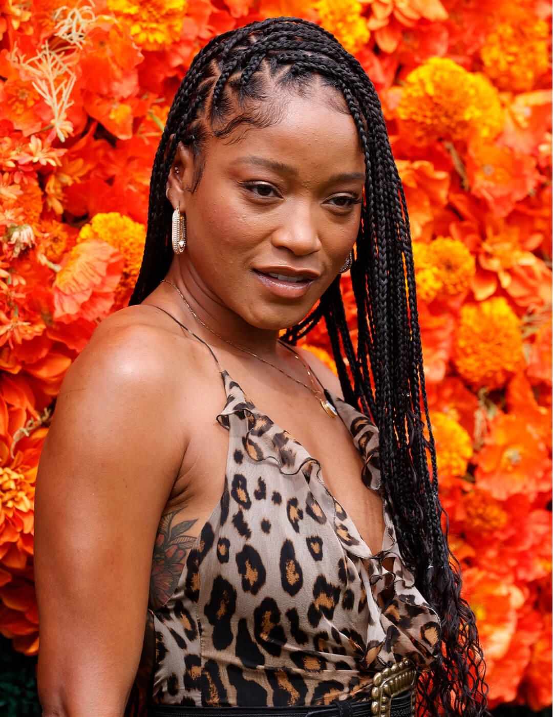 Keke Palmer rocking a side part braided hairstyle and leopard print dress against orange flowers Desktop