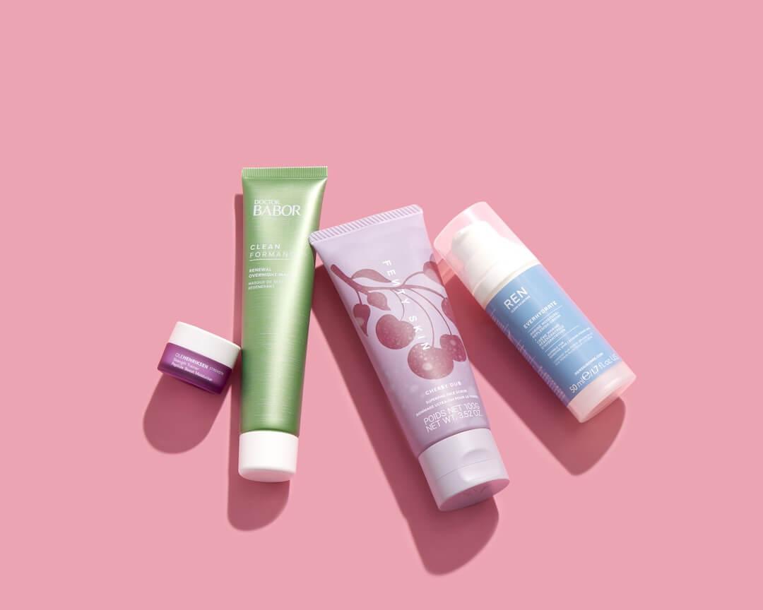 Skincare products from various brands scattered on pink background Desktop