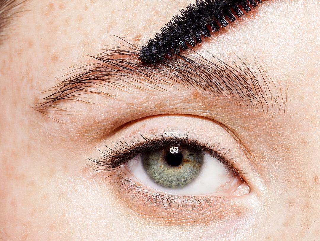 Close-up of a woman with blue-gray eyes with eyebrow getting groomed by a spoolie Desktop