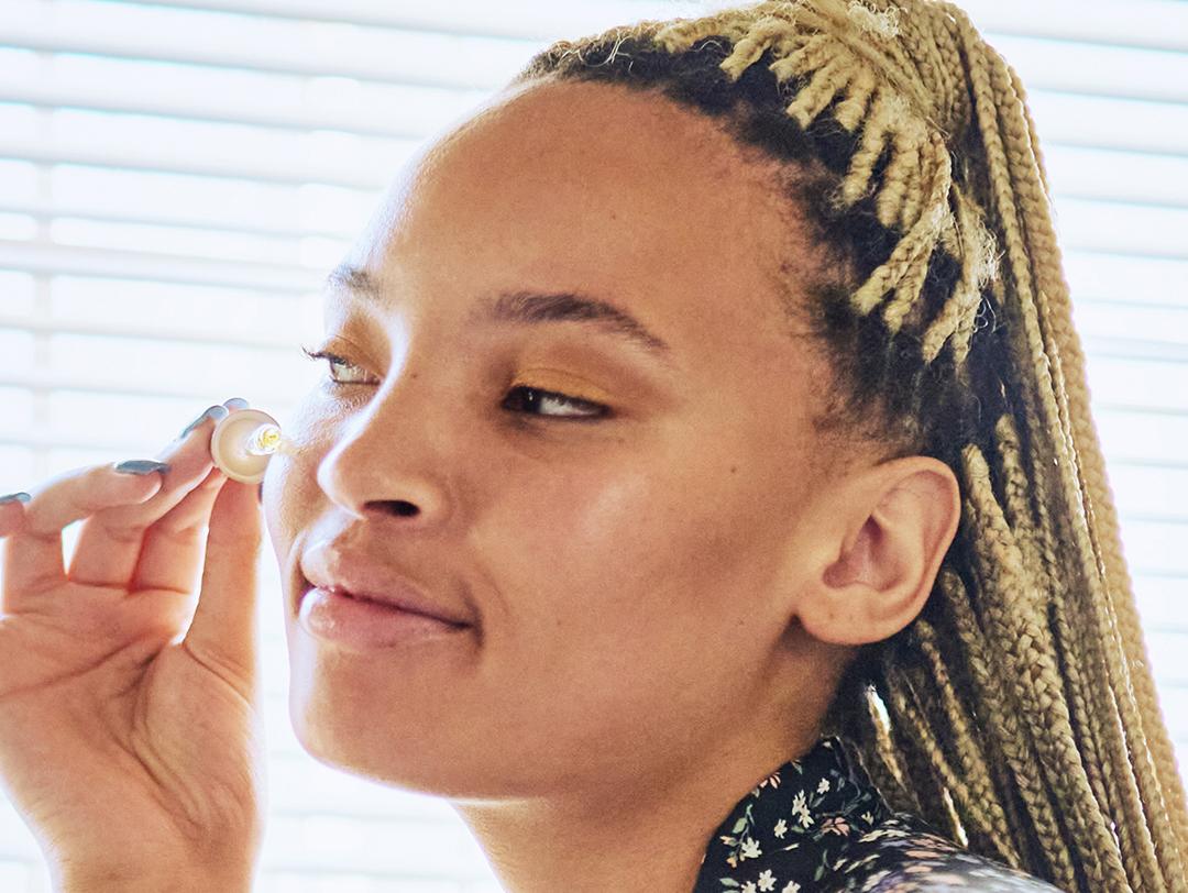 Photo of a woman with blonde braids applying serum on her face Desktop