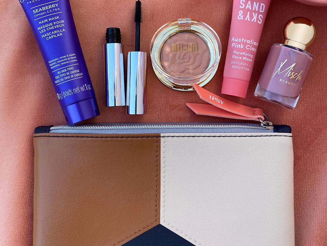 Flat lay image of the IPSY November 2020 Glam Bag along with skincare, nail, and makeup products on dark peach textile background Desktop
