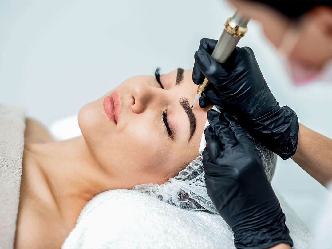 A professional beautician in black gloves carefully performs an ombré eyebrow procedure on a client with eyes closed and perfectly shaped brows, highlighting the precision and care that make this style so popular Desktop