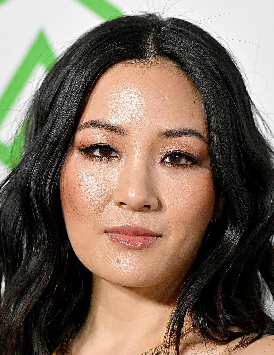 A close-up image of Constance Wu featuring her black wavy hair, subtle makeup emphasizing her hooded eyes with black eyeliner, and the gold necklace adorned with gems around her neck Desktop