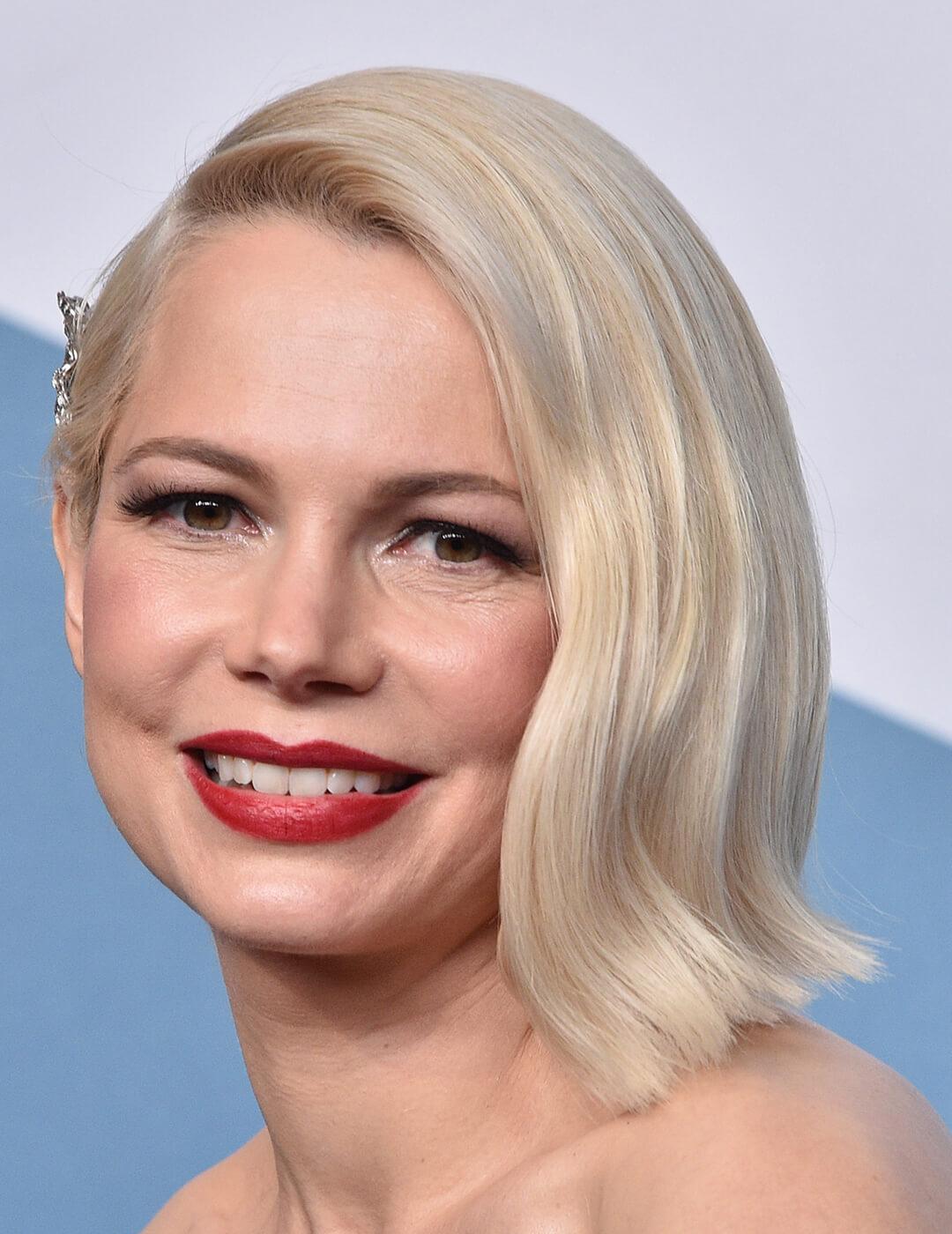 An image of Michelle Williams wearing a bold red lipstick with her hair tucked on the side of her face Mobile