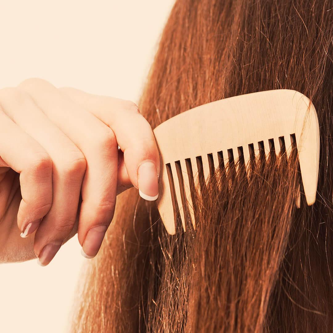 Close-up of a woman's hand combing her brunette hair with a wooden comb Desktop