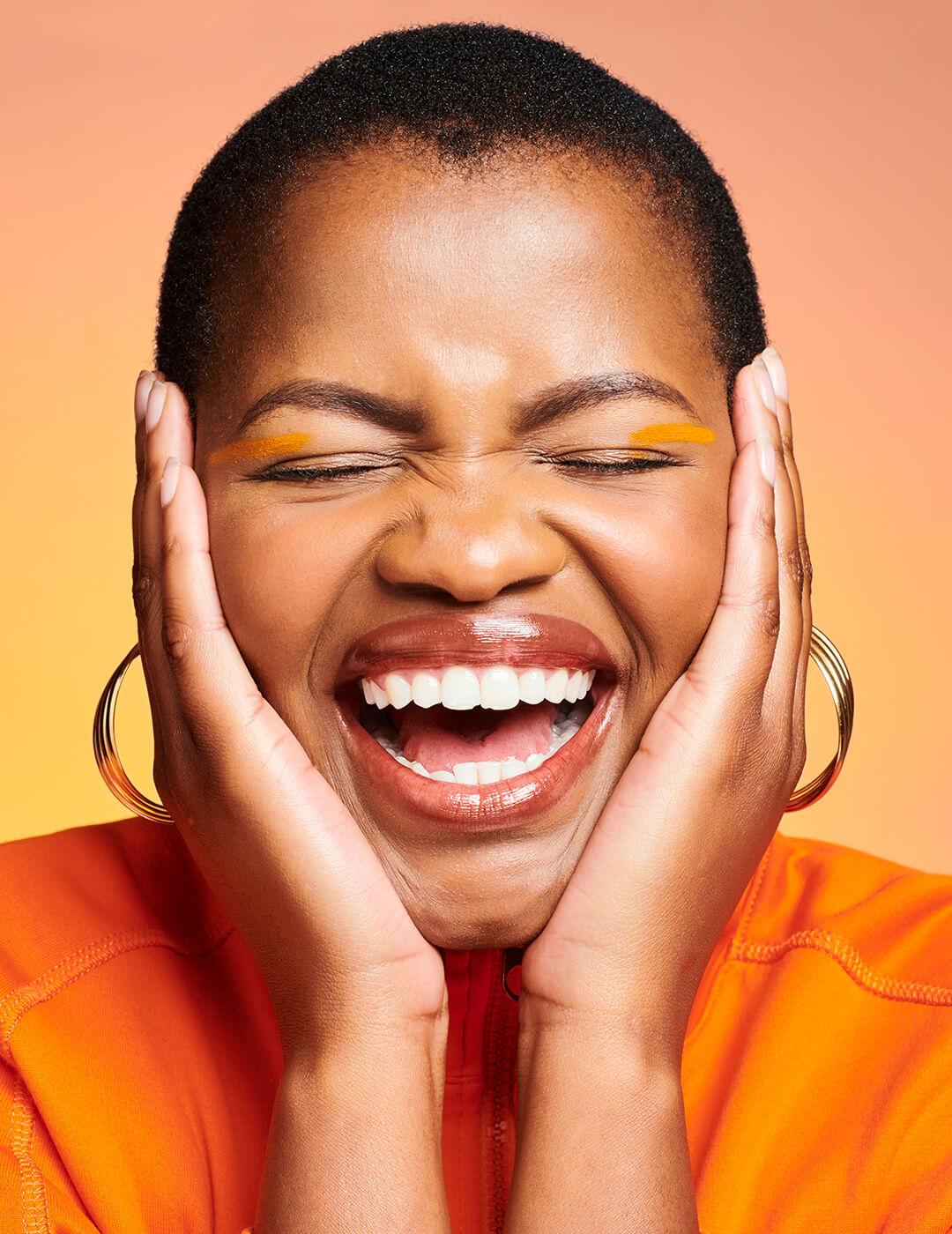 Closeup of a happy, excited and smiling African woman looking cheerful and beautiful while posing against an orange background. Face of one joyful, gorgeous and pretty black female Mobile