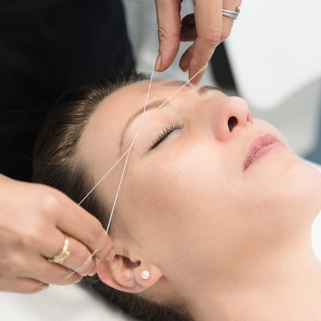 Image of a woman's hands threading another woman's eyebrow Desktop