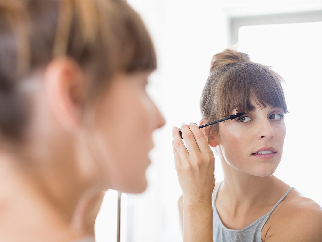 Young woman applying mascara while looking at herself in the mirror Desktop