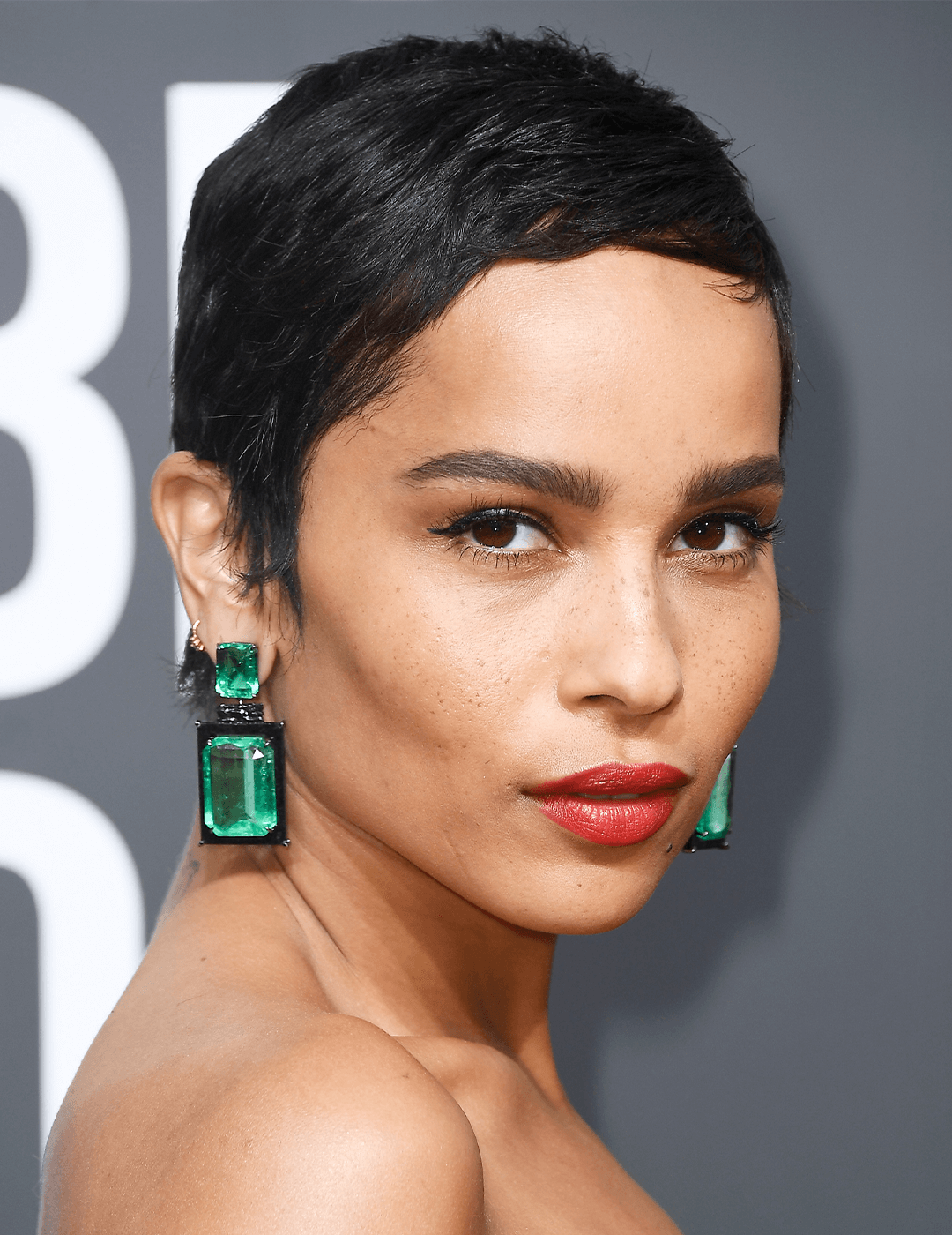 Zoe Kravitz rocking a short pixie cut hairstyle, dangling emerald earrings, and red lips makeup look Mobile