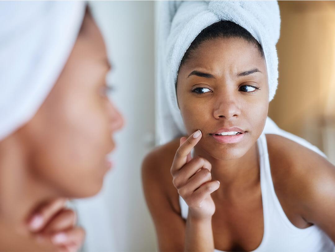Close-up of a Black woman with towel-wrapped hair checking her face in the mirror Desktop