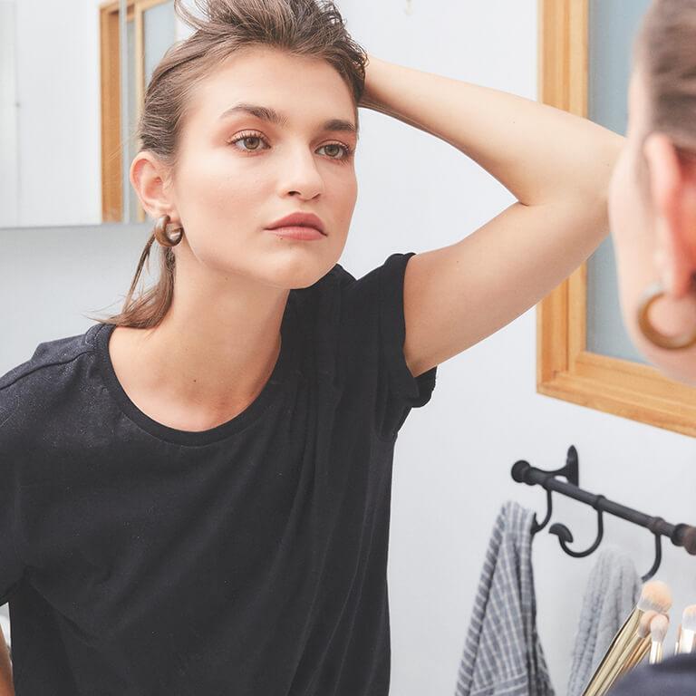 A girl in black shirt looking at herself in the mirror while holding her hair back Desktop