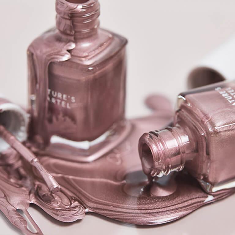 A closeup image of a model's hands with light pink graphic mani holding a light pink and black graphic bag and an image of two bottles of rose gold nail polish spilt Mobile
