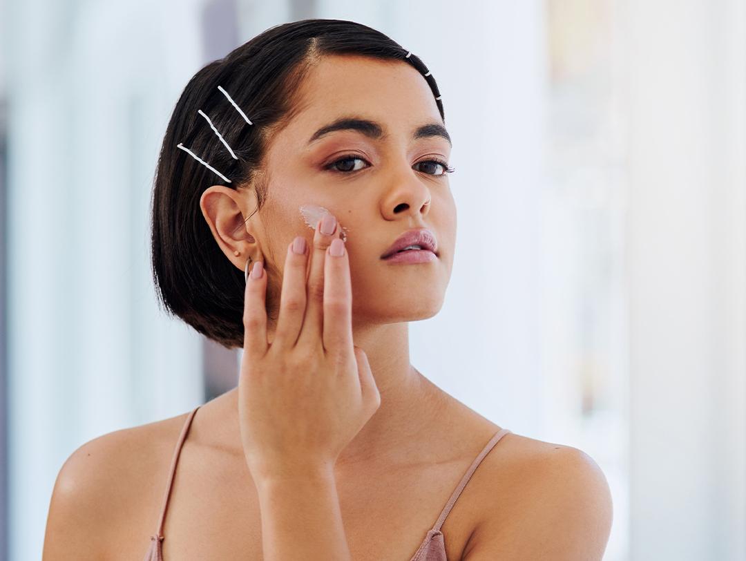 An image of a woman applying moisturizer in front of a bathroom mirror Desktop
