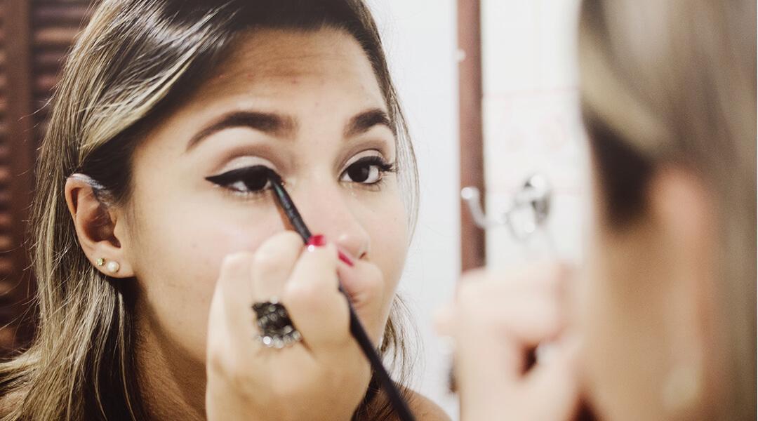 Image of a woman applying eyeliner while looking at herself in the mirror Desktop