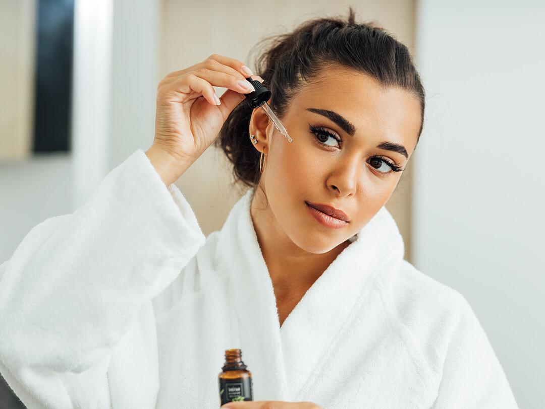 Close-up of a beautiful woman in a white bathrobe applying serum on her face with a dropper Desktop