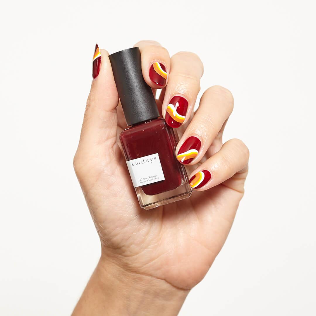 Image of a model's hand with colorful nail art holding the SUNDAYS Nail Polish in No. 18 Mobile