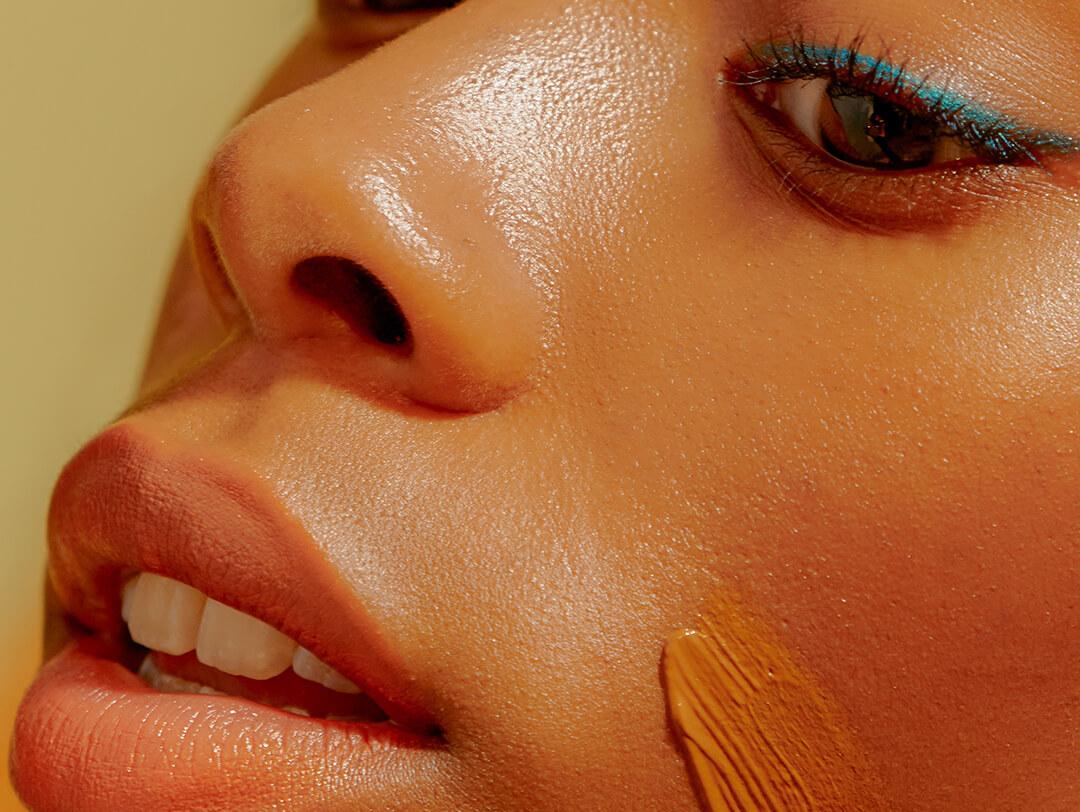 Young woman with a blue eyeliner makeup look applying foundation on her face Desktop
