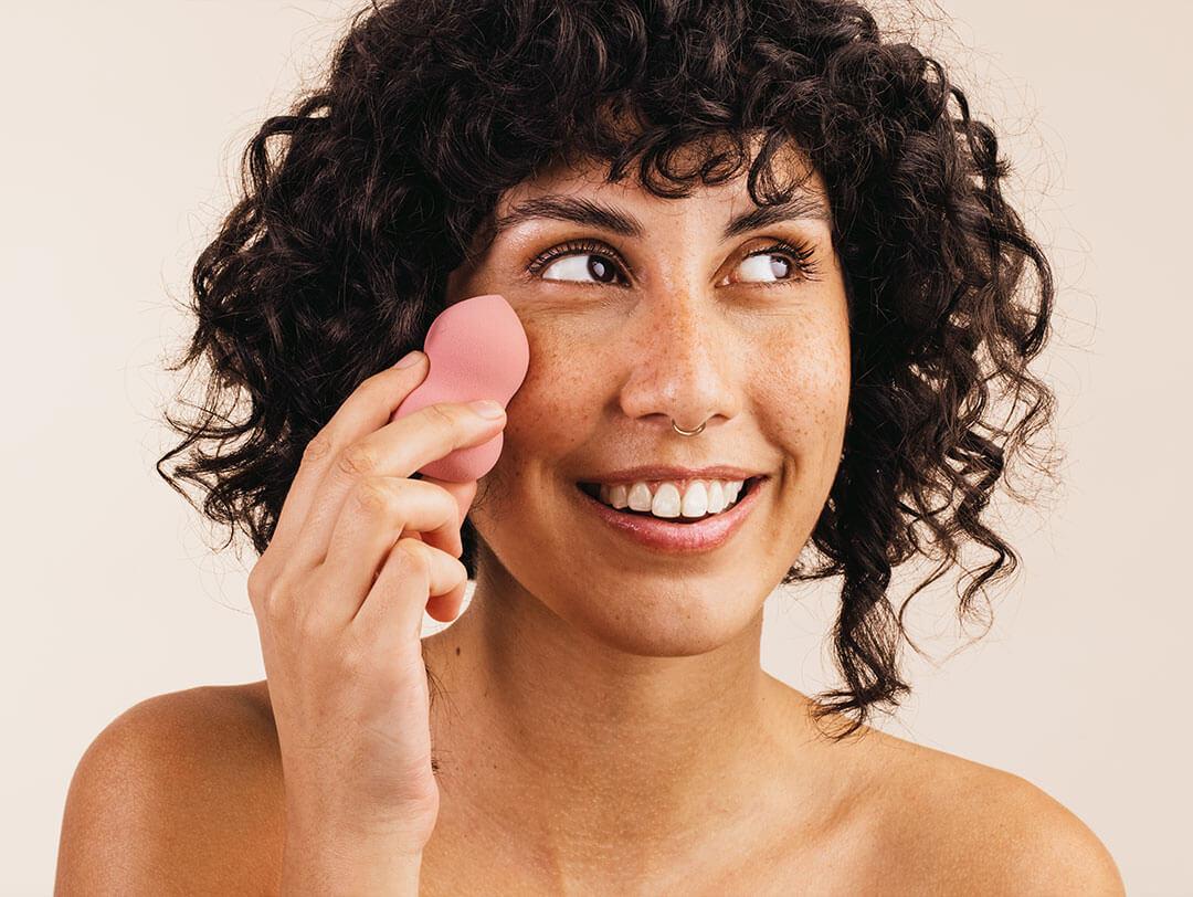 An image of a women using a pink sponge to apply something to her face Desktop
