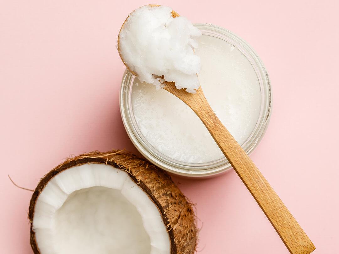 Coconut half, jar of coconut oil, and wooden spoon on pink background Desktop