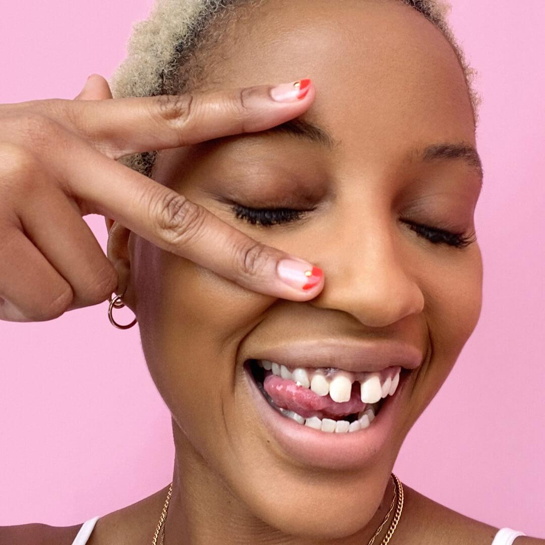 Close-up of a Black model making a wacky face and showing her red and gold nail art Desktop