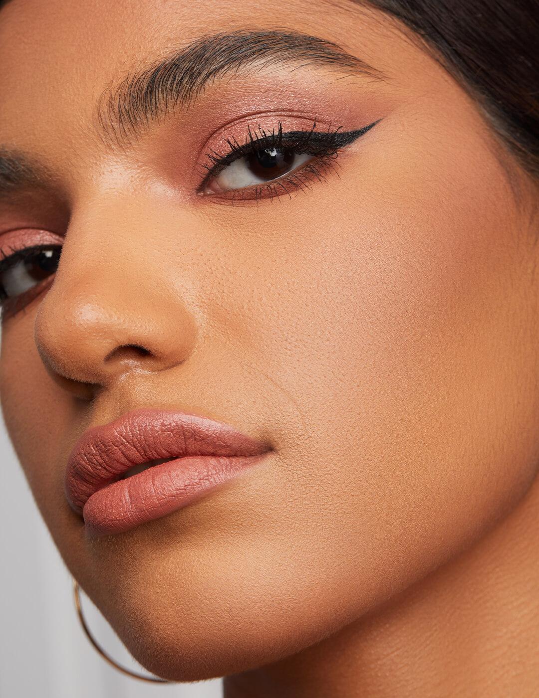 Close-up of a model rocking shimmery a rose gold eyeshadow and winged eyeliner look and nude pink lips Desktop