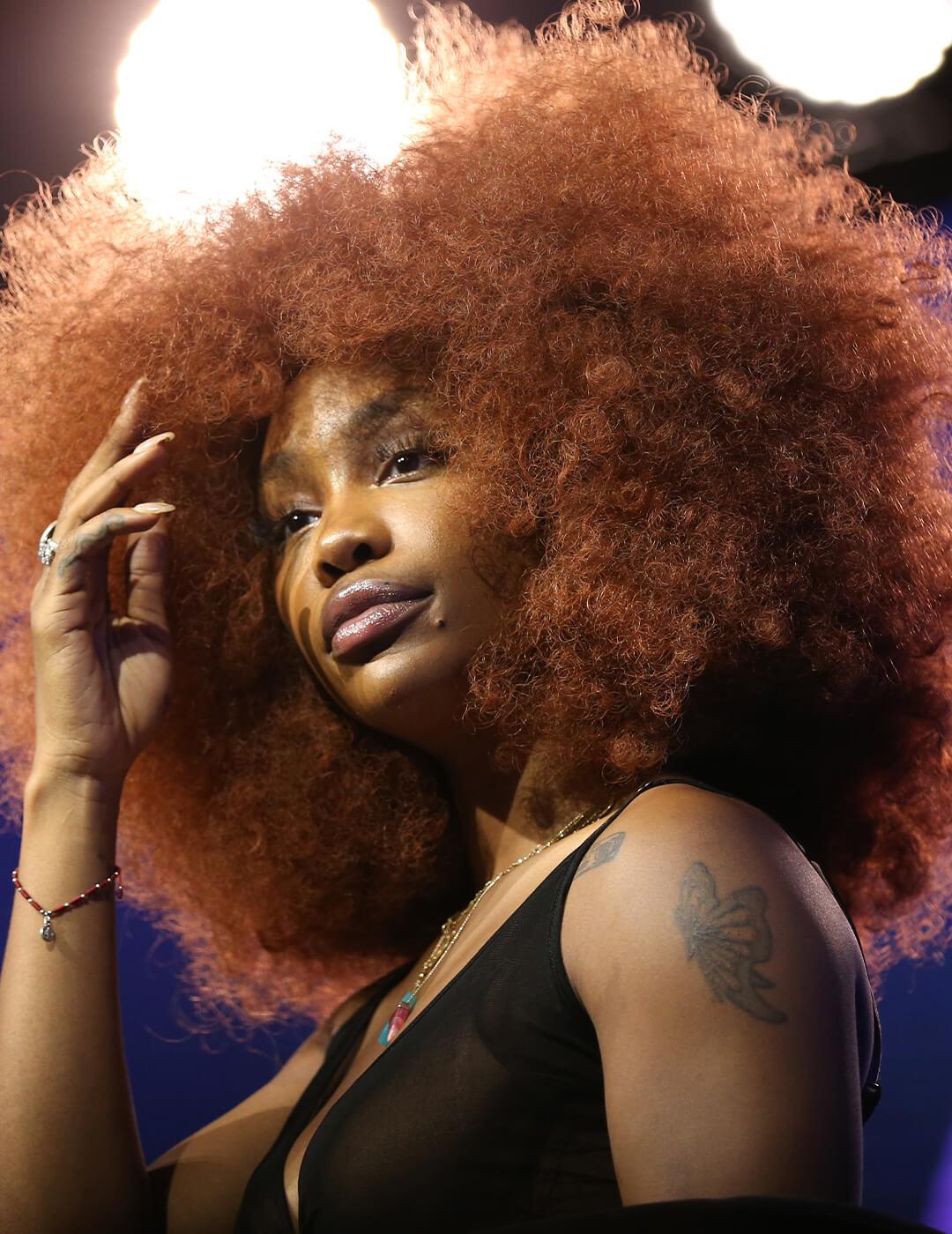 A photo of SZA with a mocha copper afro hair and wearing a black dress Desktop