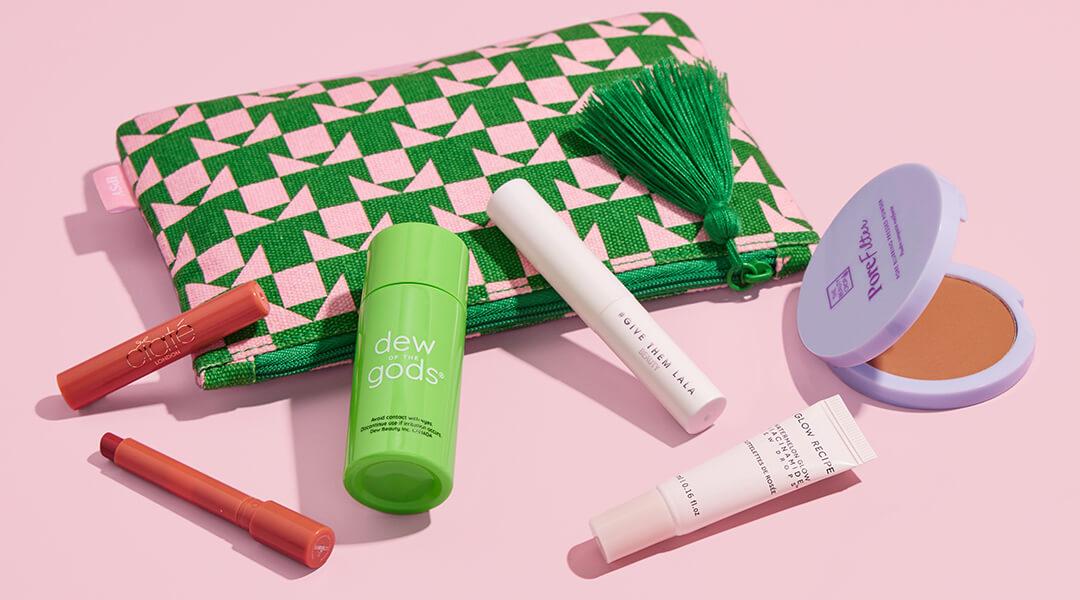August 2023 IPSY Glam Bag with beauty products from various brands on pink background Desktop