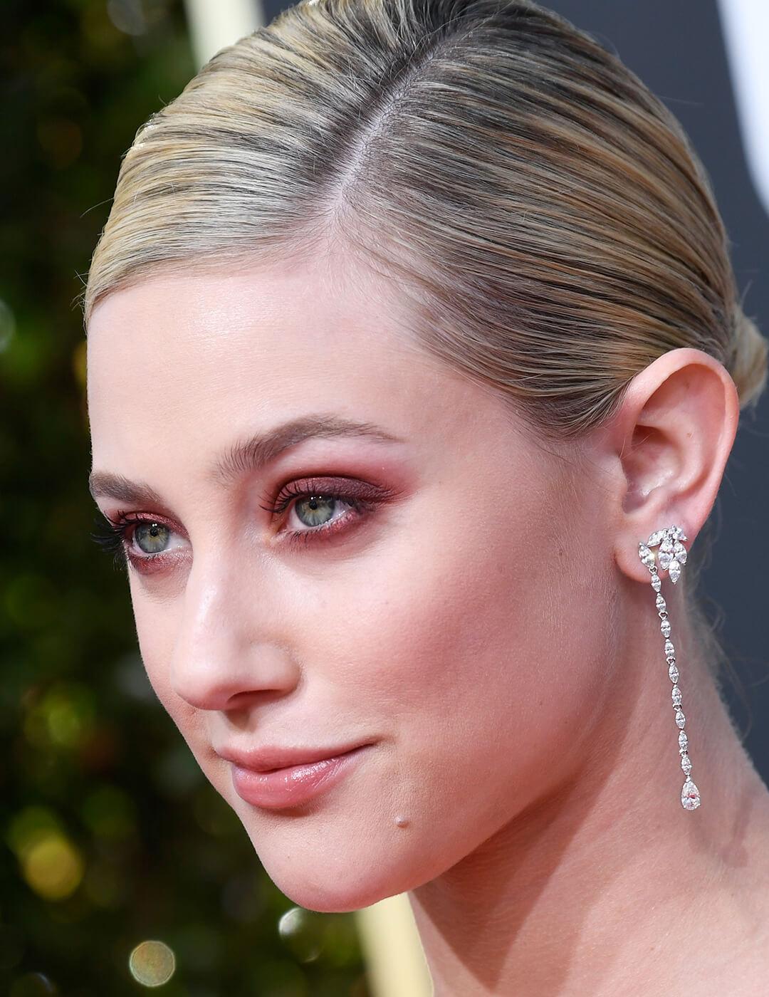 Close-up of Lili Reinhart rocking a slick back hairstyle, soft red smoky eye makeup, and silver dangling earrings Mobile