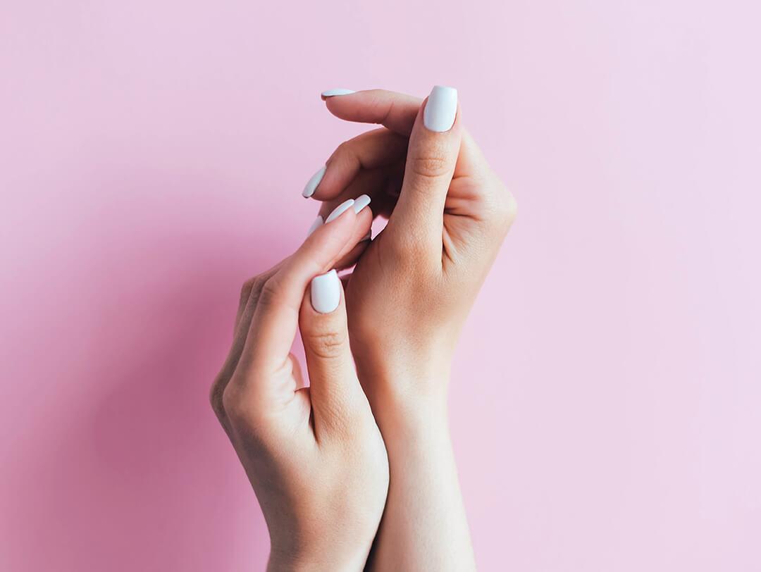 Close-up of woman's hands with white nail polish against pink background Desktop