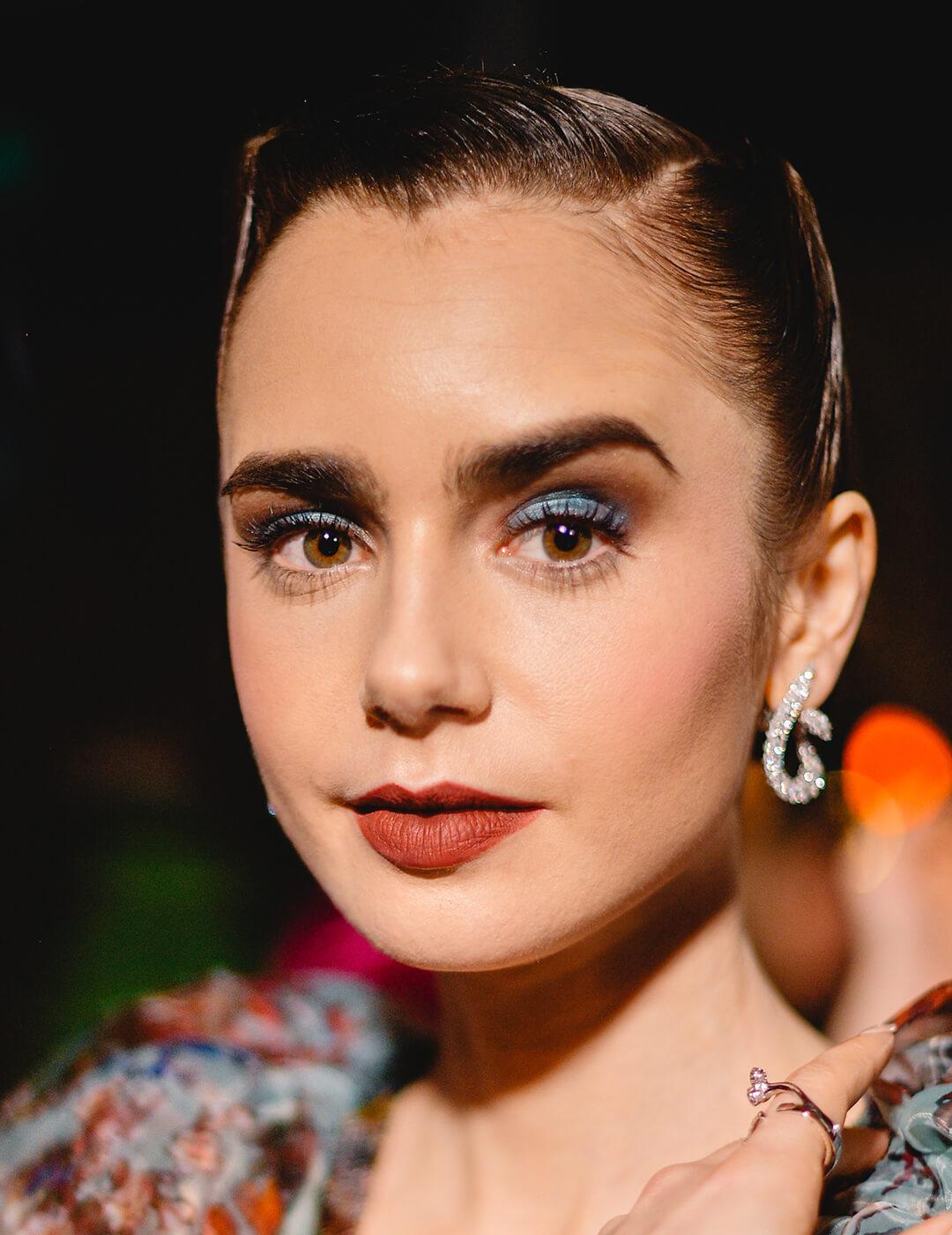 Lily Collins looking glam in a sleek hairstyle, blue smoky eyeshadow makeup look, and floral dress Mobile