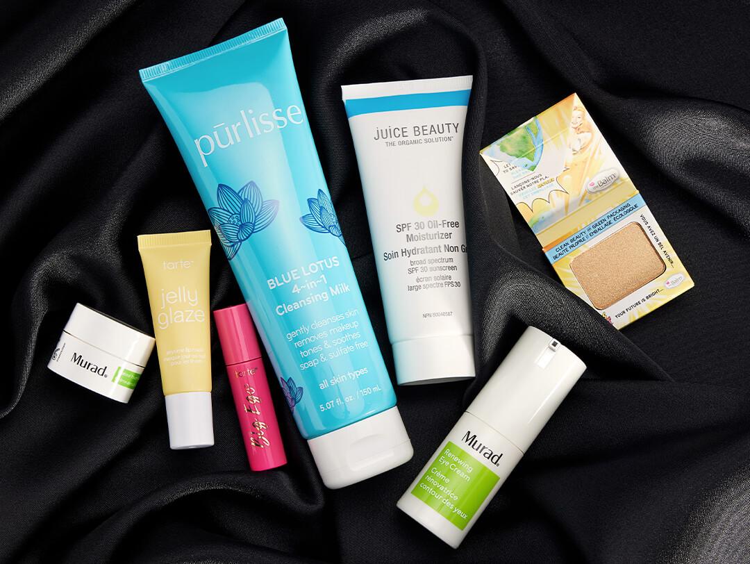 Skincare and makeup products from various brands scattered on black silk cloth Desktop