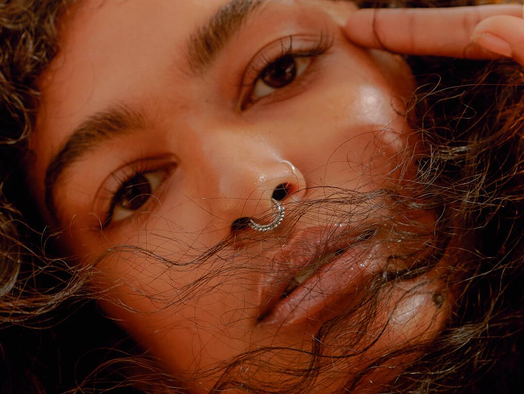 A closeup photo of a model with curly hair and a nose pricing Desktop