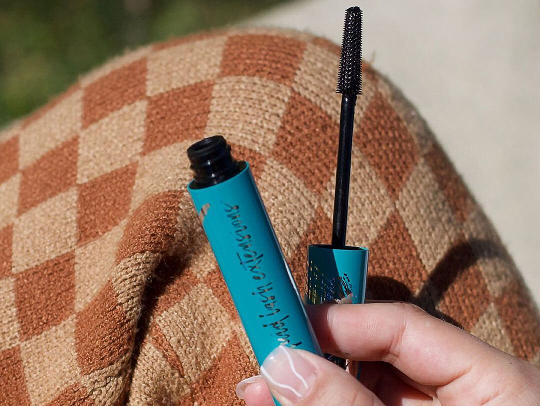 Close-up of woman's hand holding a THRIVE CAUSEMETICS mascara on brown checked cloth Desktop