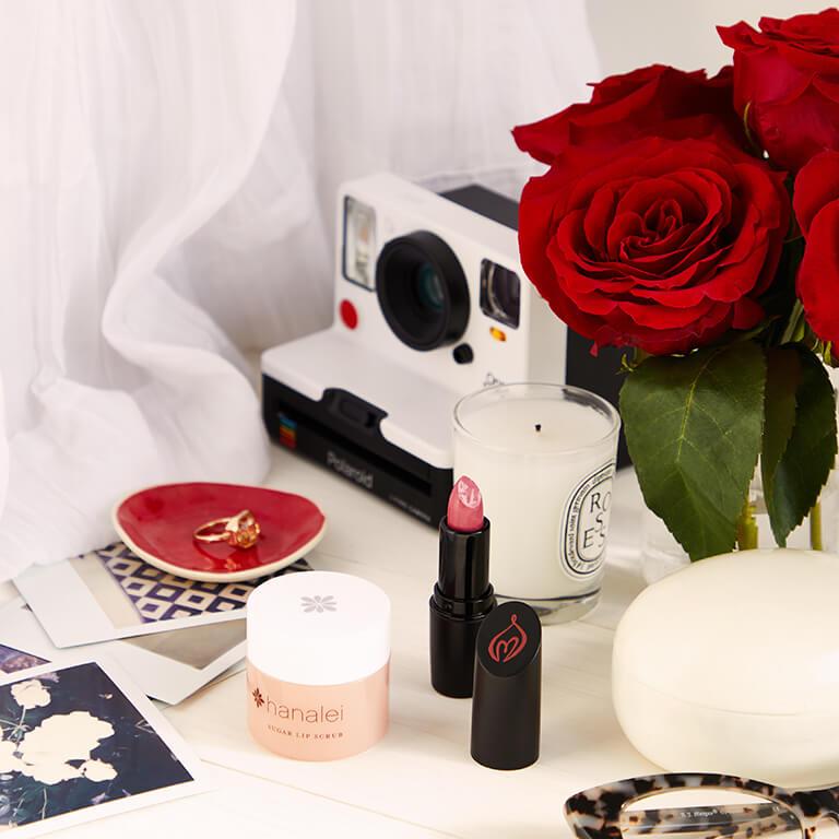 A image of lip products, candle, polaroid camera, roses, and a ring in a saucer Desktop