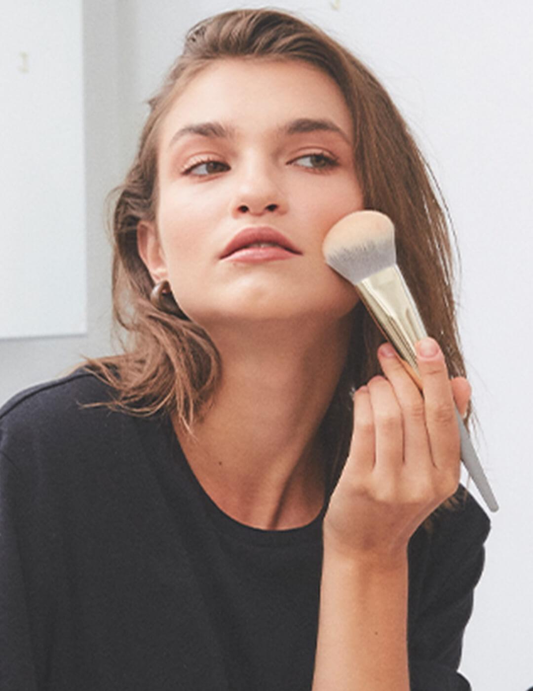 A photo of a woman wearing black top holding a powder brush pressed against her cheeks Mobile