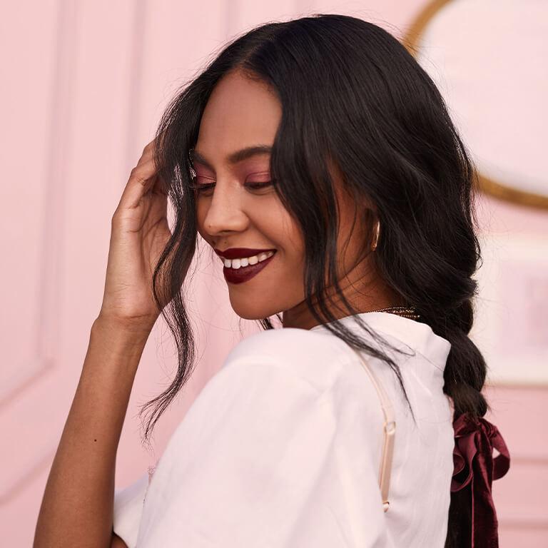 A profile image of a model with loose braids having a rose gold eyeshadow look and dark berry lipstick Desktop